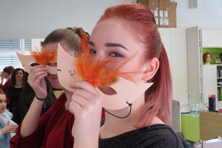 Udeleženka modnega dogodka z oranžnim pernatim dodatkom na obrazu.